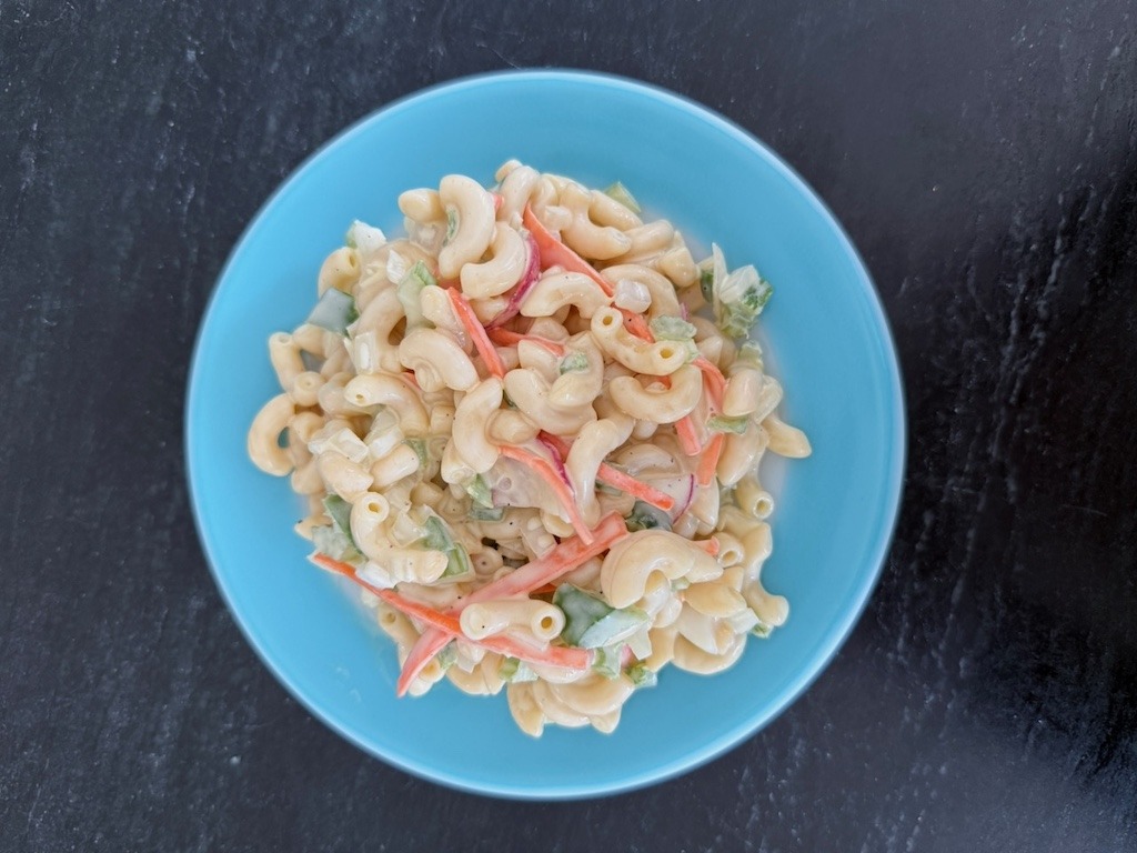 Overhead view of macaroni salad with radishes, carrot and green pepper in a blue bowl