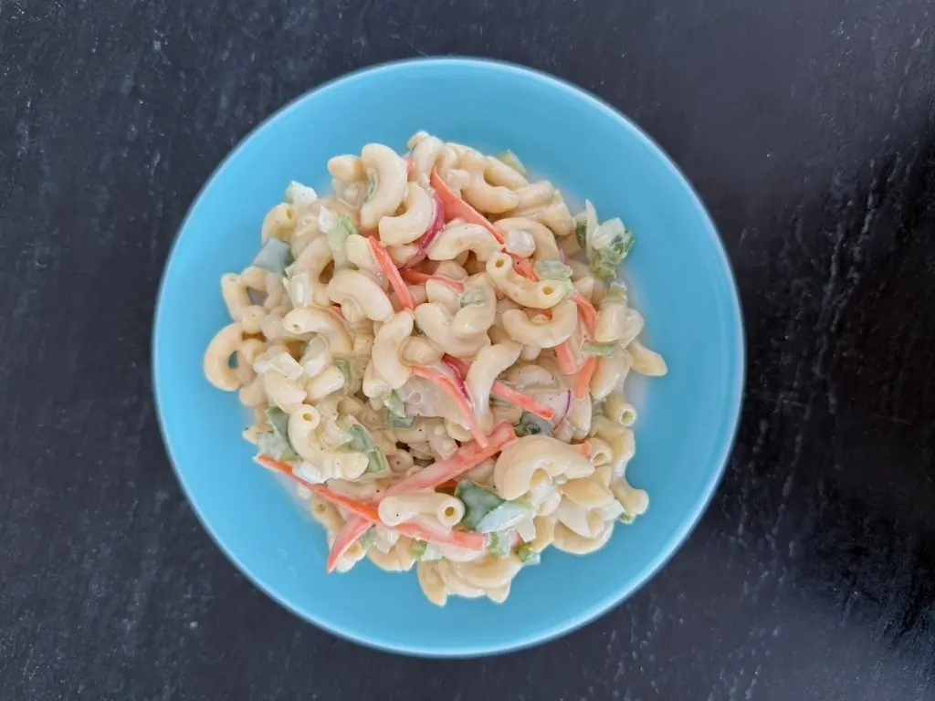 Overhead view of macaroni salad with radishes, carrot and green pepper in a blue bowl