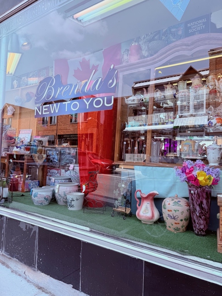 Addressing myths about thrifting. Storefront window of Brenda's New to You secondhand shop in Almonte Ontario displaying colourful ceramic vases pitchers and vintage housewares