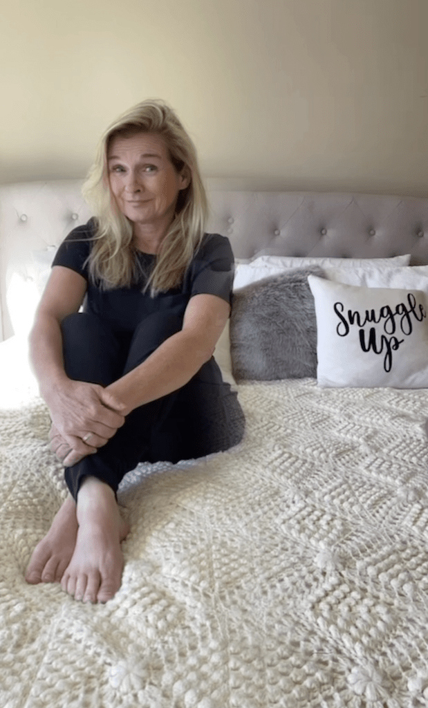 Woman sitting on a bed covered in a large cream handknitted king size blanket talking myths about thrifting