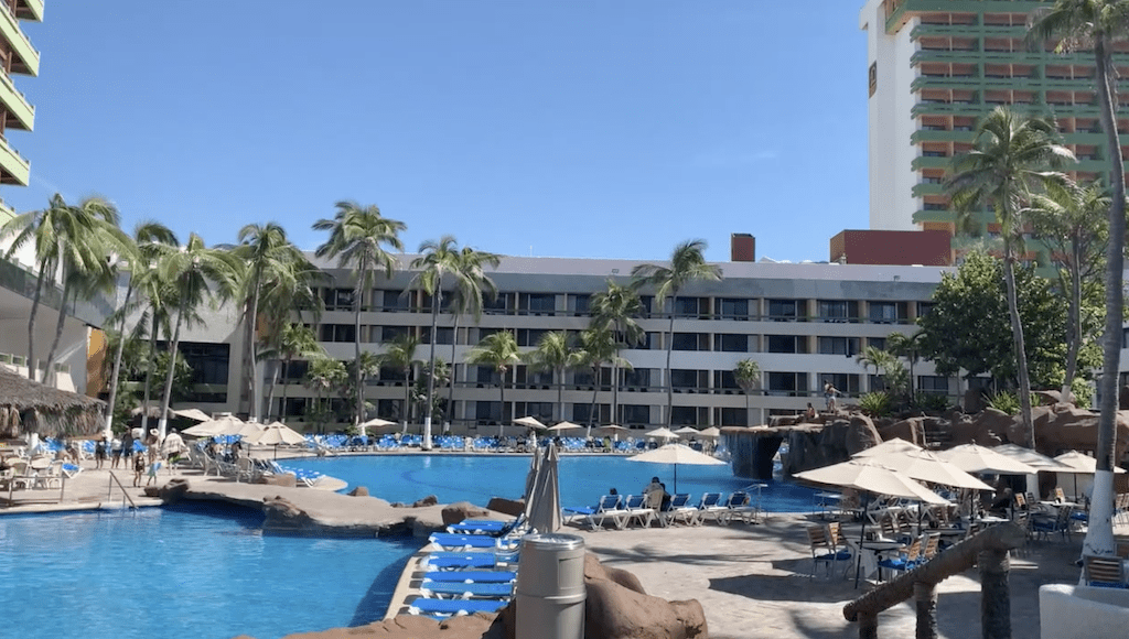 Large outdoor pool at El Cid El Moro Beach Resort in Mazatlán Mexico surrounded by palm trees and lounge chairs