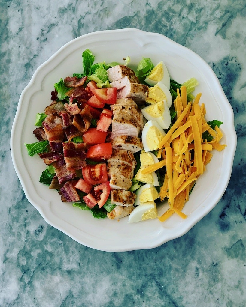 A plate with Cobb Salad made with hard boiled eggs, bacon, tomatoe and cheese