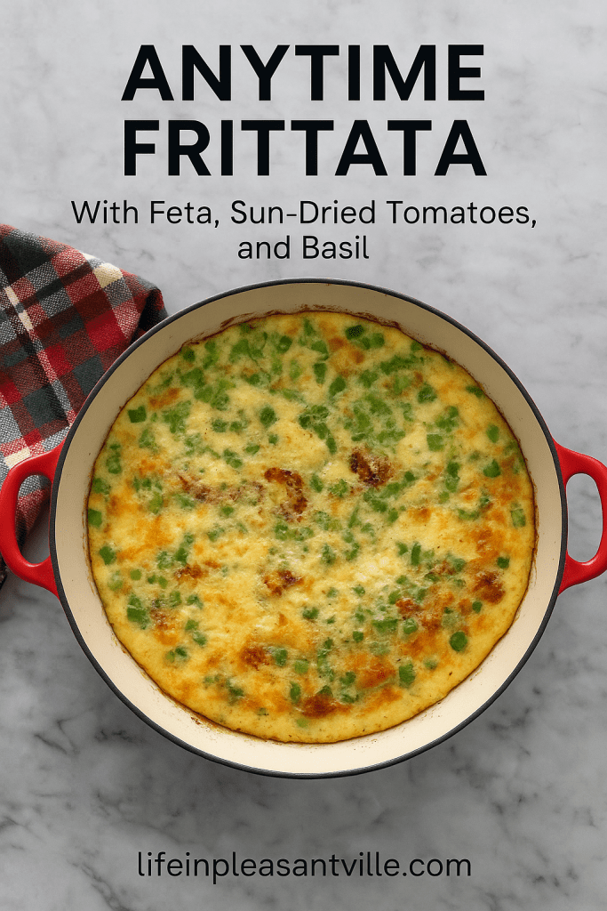 Overhead view of a baked frittata in a red-handled skillet with green onions, sun-dried tomatoes, and feta, set on a marble countertop with a plaid napkin. Text overlay reads "Anytime Frittata with Feta, Sun-Dried Tomatoes, and Basil – lifeinpleasantville.com"