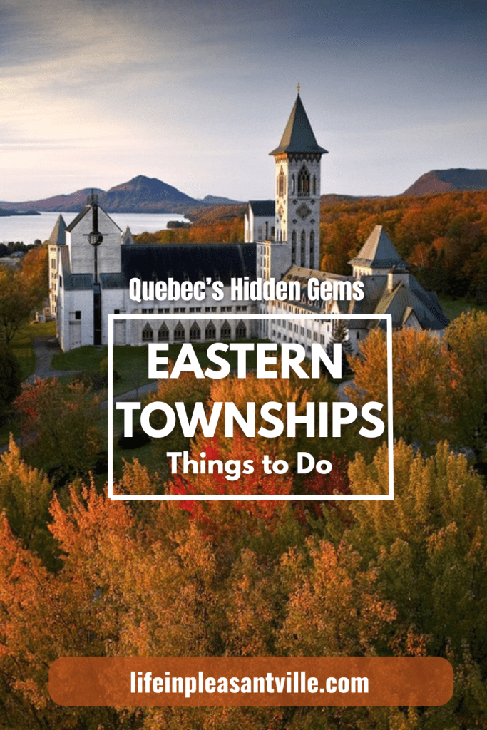 A drone shot of the Abbaye Saint-Benoît-du-Lac surrounded by vibrant fall foliage in Quebec’s Eastern Townships, with a mountain and lake in the background.
