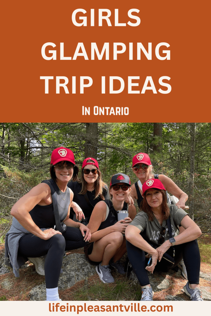 Group of women on a glamping trip in Ontario, smiling in hiking gear and matching red hats, surrounded by forest.