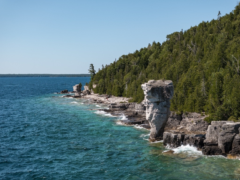 Turquoise waters and limestone cliffs along the coast of Bruce Peninsula National Park, with the iconic Flowerpot Rock surrounded by lush green forest.