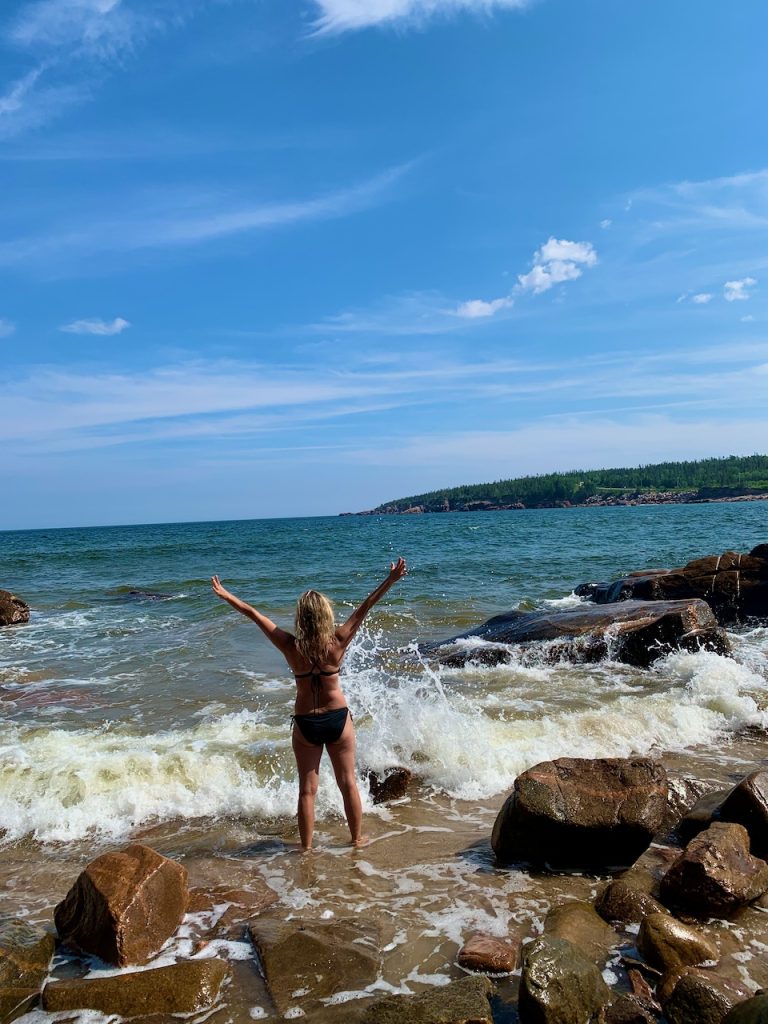 Woman wading into the ocean on a Canadian East Coast beach, embracing nature and summer travel in Canada