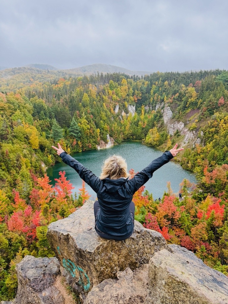 Woman raising her arms triumphantly over a scenic lookout for a Cabot Trail fall road trip.