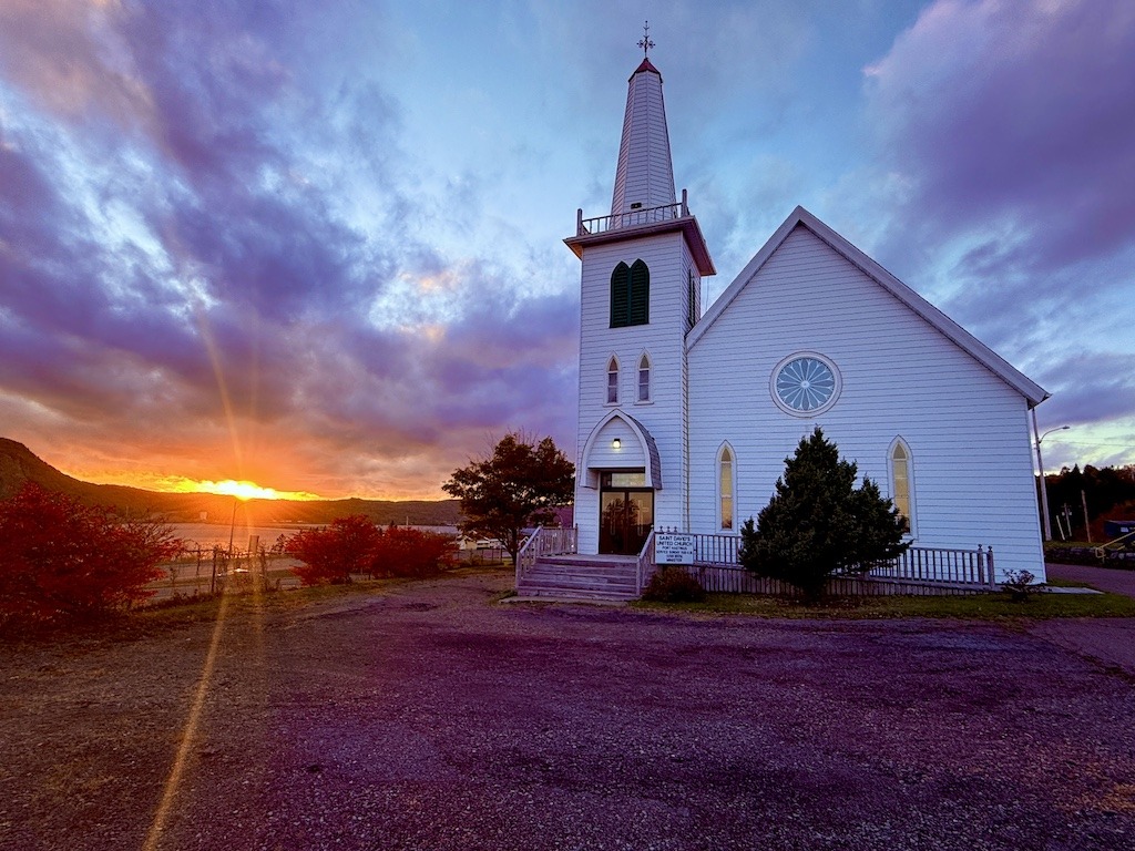 A church with a sunset in the background that begins to explain a Cabot Trail fall road trip itinerary.