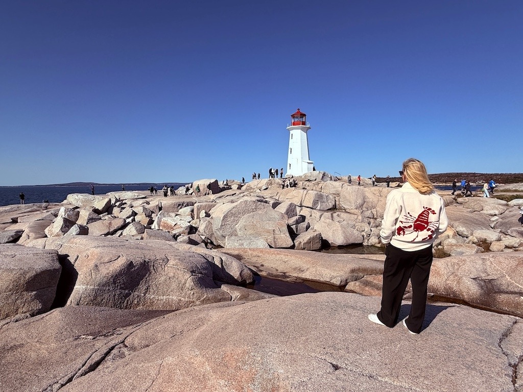 Woman standing on rocks looking at Peggy’s Cove lighthouse in Nova Scotia during a Canada Strong Pass trip