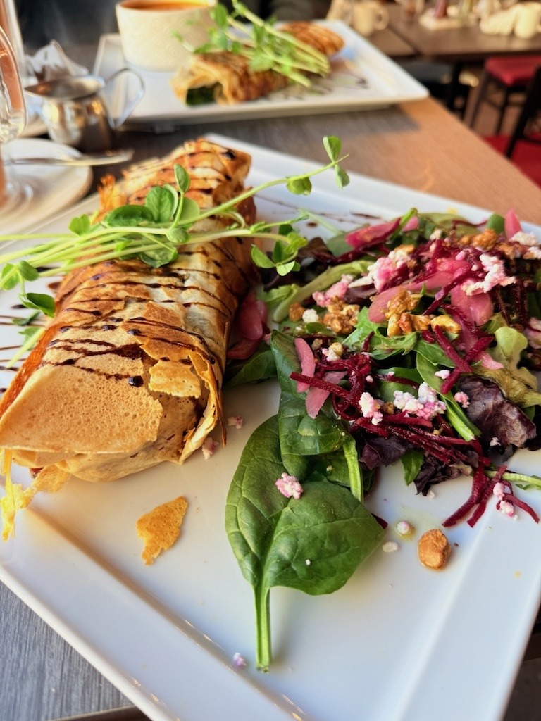 Close-up of a savoury cherry chicken crepe drizzled with balsamic glaze, served with a side salad of mixed greens, shredded beets, goat cheese, and toasted nuts at Mill Street Crepe Company.