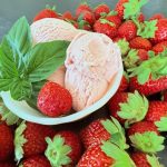 Bowl of homemade strawberry basil ice cream with fresh strawberries and basil on a dark background