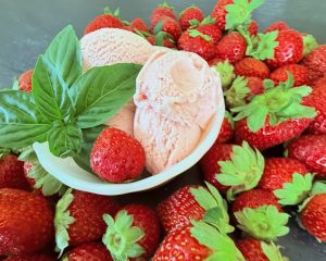 Bowl of homemade strawberry basil ice cream with fresh strawberries and basil on a dark background