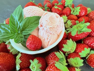 Bowl of homemade strawberry basil ice cream with fresh strawberries and basil on a dark background