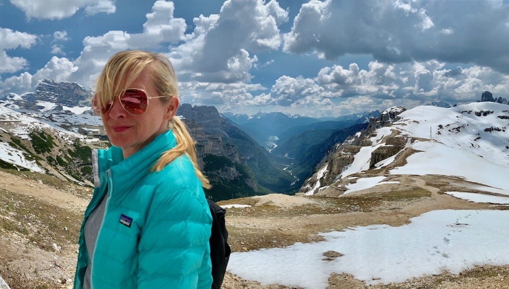 Woman standing in the Italian Dolomites surrounded by snow-capped mountains, rediscovering the natural world one trip at a time