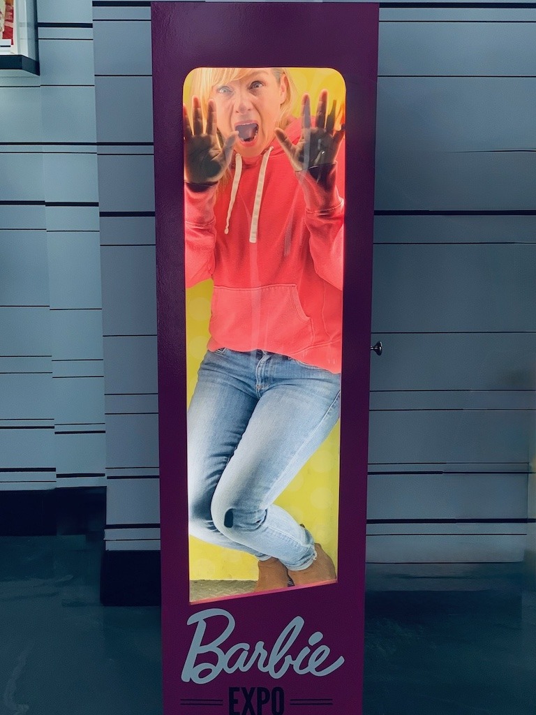 Gen X woman trapped in a Barbie box at Barbie Expo, a metaphor for the impossible standards women were sold