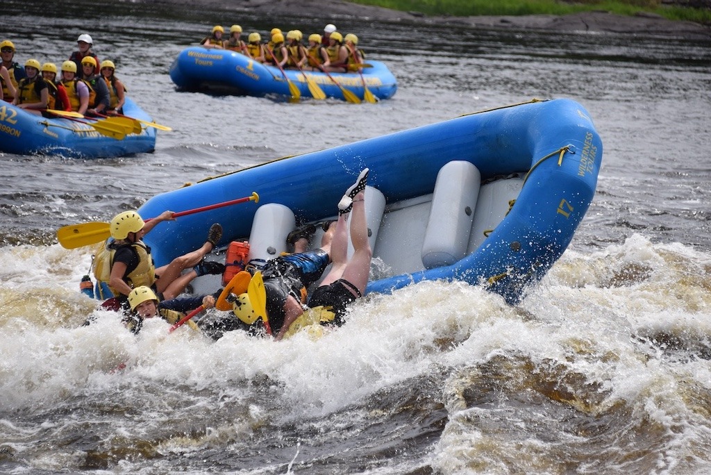 Group of women getting flipped in a white water rafting raft, the kind of messy real-world adventure extinction of experience puts at risk.