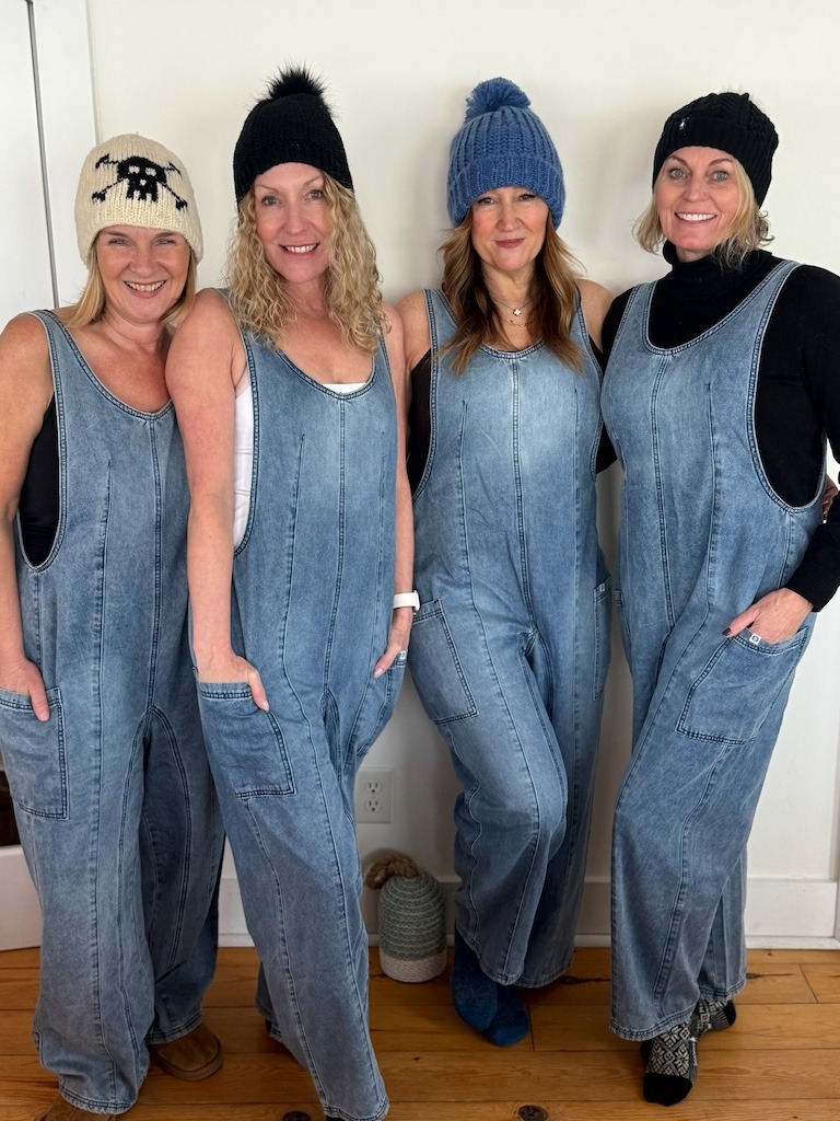 Four women in matching denim overalls and winter hats