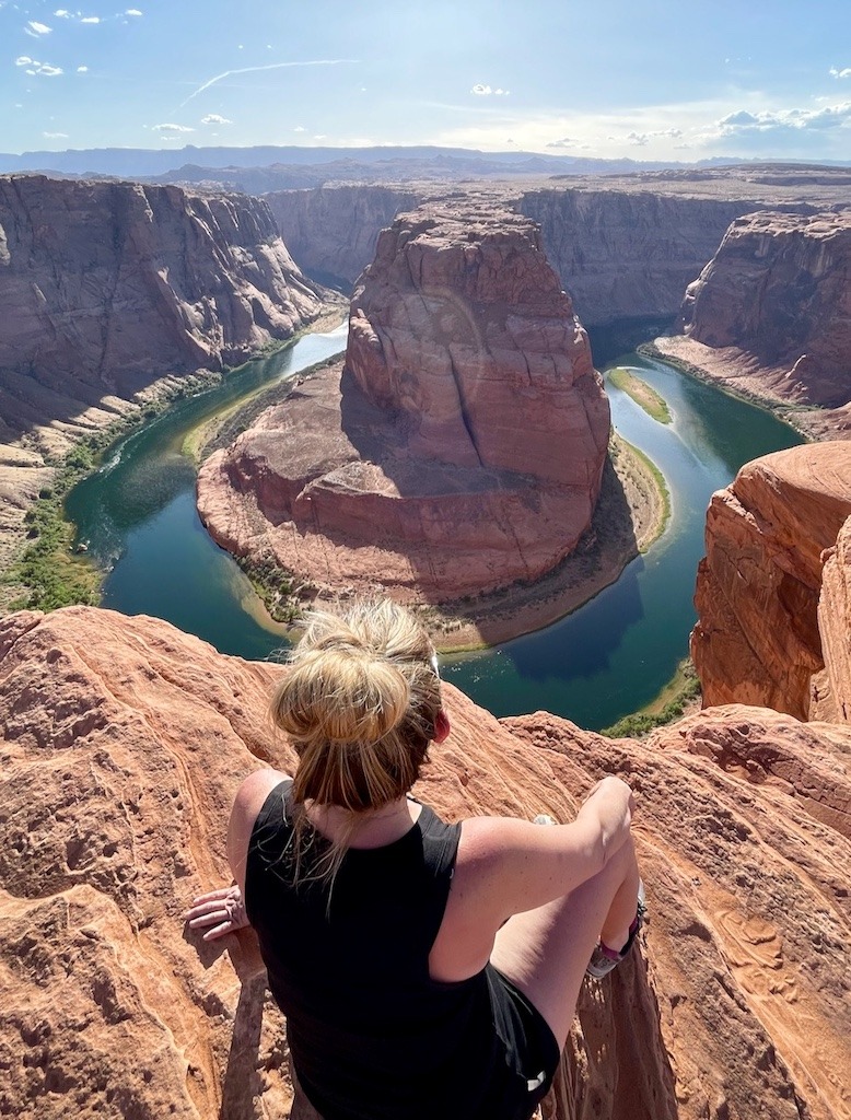 Woman sitting alone at the edge of Horseshoe Bend canyon, fully present in the natural world without a phone in sight.