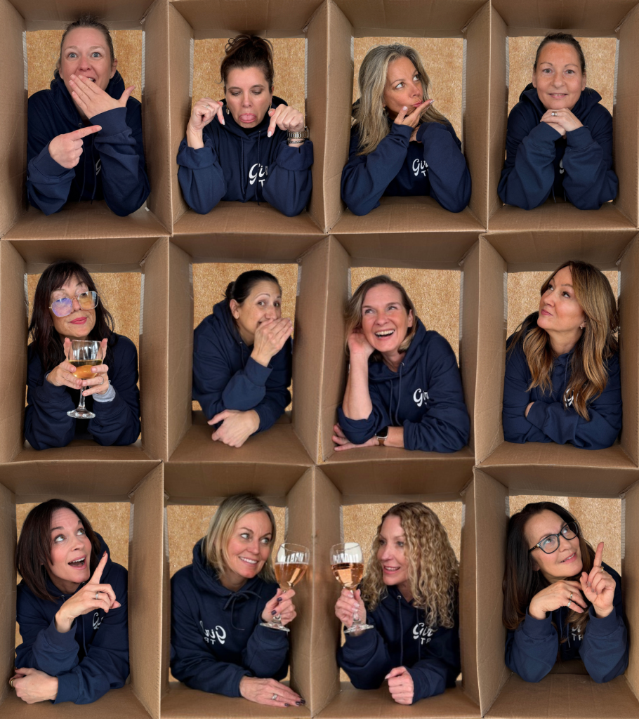 Women in matching navy hoodies posing playfully inside cardboard box cubbies during a girls weekend retreat.