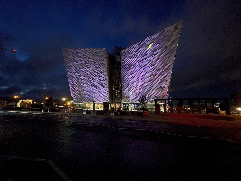 Titanic Belfast museum illuminated at night, its distinctive ship-bow architecture lit in purple against a dark sky, Belfast, Northern Ireland.