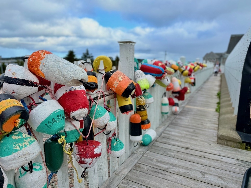 Colourful fishing buoys hanging on a white fence along a wooden boardwalk in Louisbourg Nova Scotia