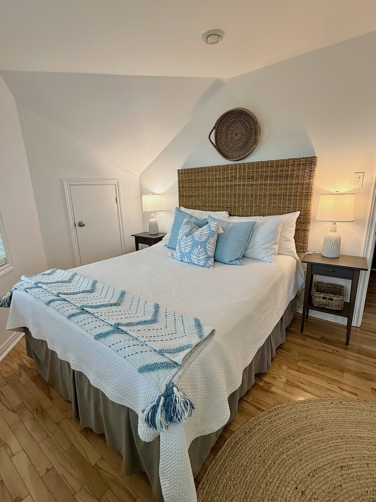 Bright, coastal-styled guest room at North Star Louisbourg with a rattan headboard, blue and white bedding and hardwood floors