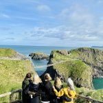 A group of travellers looking out over Carrick-a-Rede rope bridge and the Causeway Coast, Northern Ireland