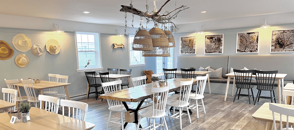 The bright, coastal interior of Coast restaurant at North Star Louisbourg with white Windsor chairs, live-edge wood tables and woven pendant lights hanging from a driftwood branch