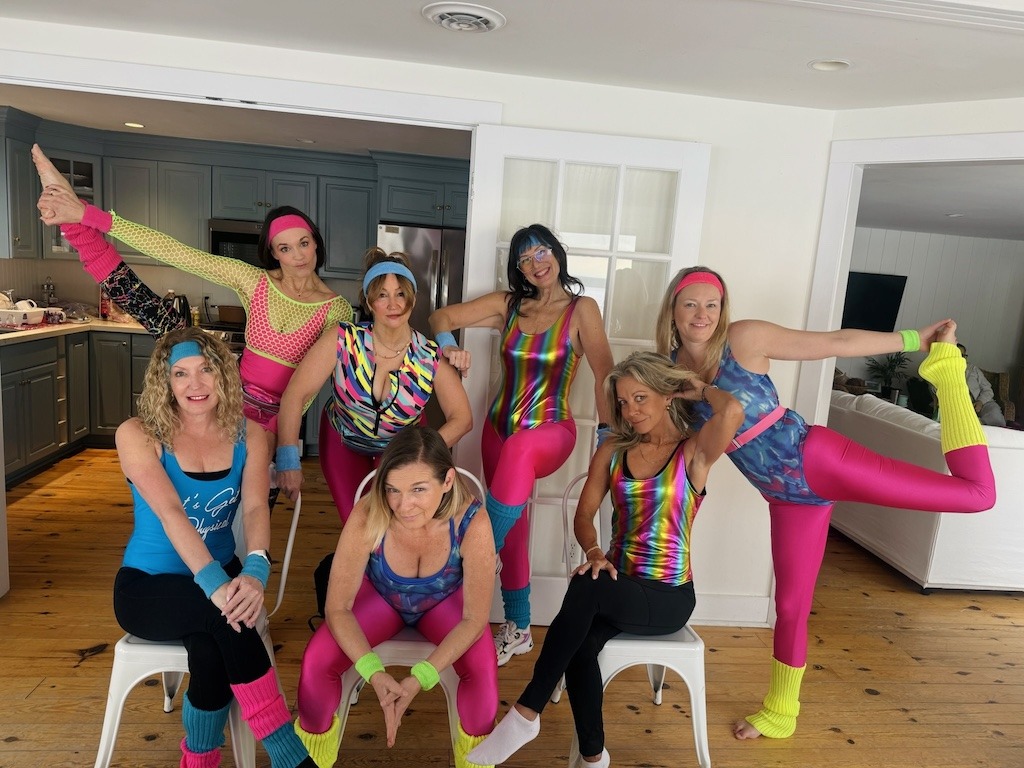 women in 80s aerobics costumes laughing together on a girls trip
