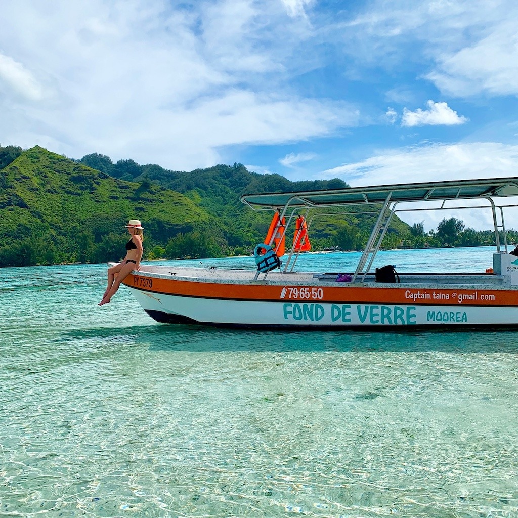 Woman sitting on boat bow in Moorea Tahiti with turquoise lagoon and green mountains