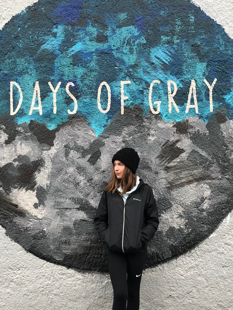 Teenage girl standing in front of Days of Gray street art mural in Reykjavik Iceland