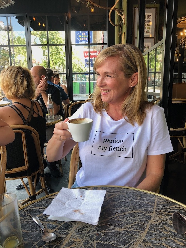 Woman wearing Pardon My French t-shirt drinking coffee at Paris café