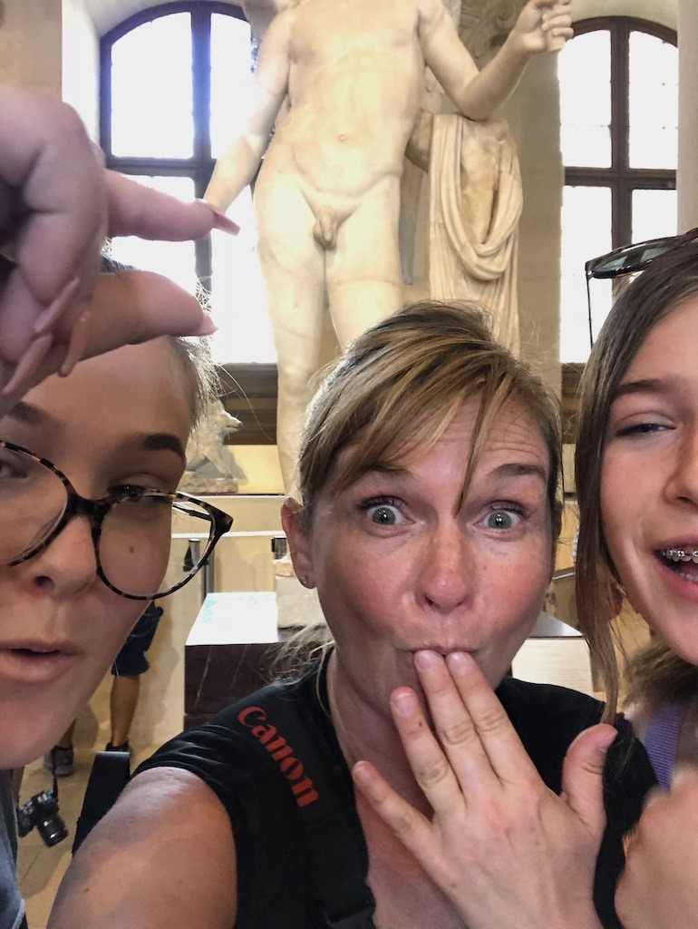 Women laughing in front of classical nude statue at the Louvre in Paris