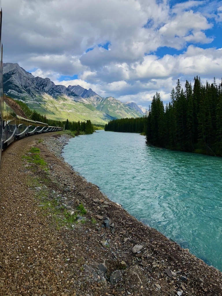Rocky Mountaineer train travelling alongside turquoise mountain river in Canadian Rockies picture in an article can travel heal a broken heart