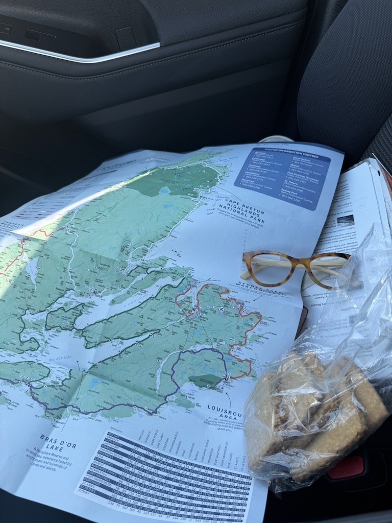 A paper map of Cape Breton on a car seat with reading glasses and a bag of oatcakes