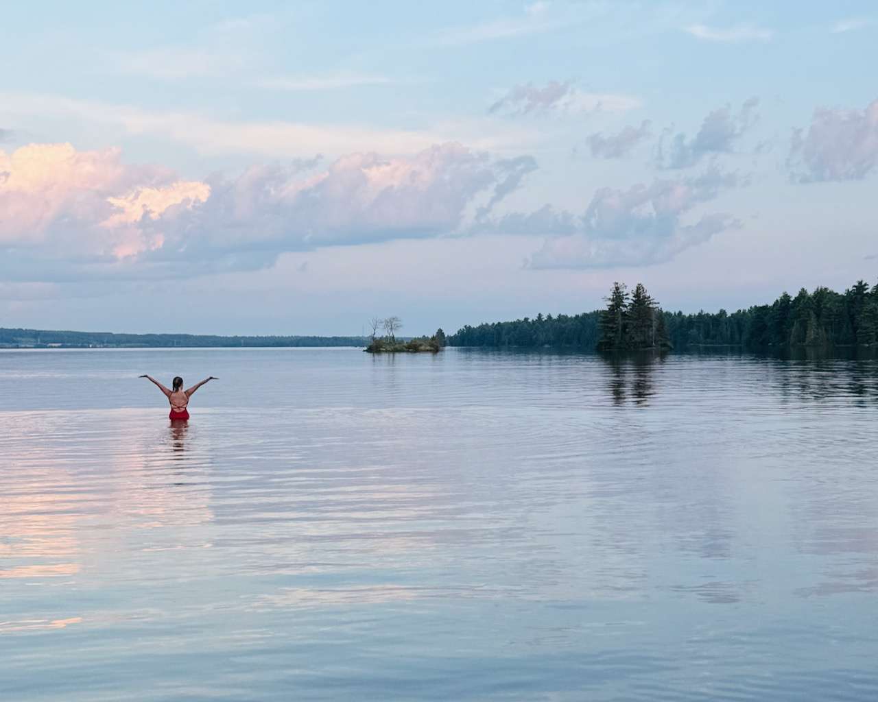 A woman standing in a calm lake at sunset, taking a quiet moment, at an Ottawa Valley summer camp for women